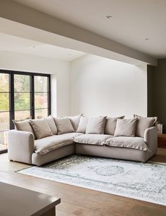 a living room with a sectional couch and large windows in the back wall, along with a rug on the floor