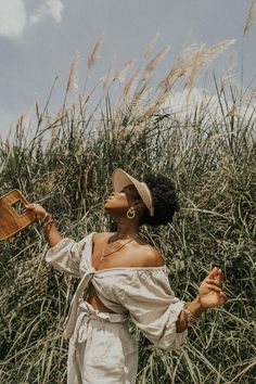 a woman standing in front of tall grass with her hands out and looking up at the sky