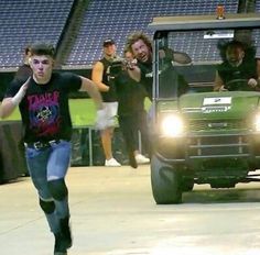 a group of people riding on the back of a green truck in front of a crowd