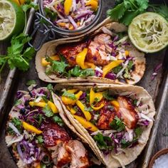 three fish tacos with cole slaw, mango salsa and lime wedges on a tray