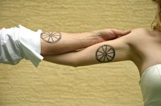 two people with tattoos on their arms holding each other's hands and one has a piece of fruit in the shape of a wheel