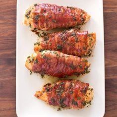 three pieces of bacon wrapped in herbs on a white platter next to a wooden table