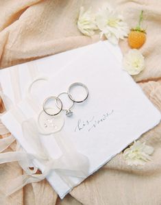 two wedding rings sitting on top of a white piece of paper next to some flowers