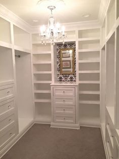 an empty walk in closet with white shelves and chandelier hanging from the ceiling