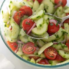 a salad with cucumbers, tomatoes and onions in a glass bowl on a table