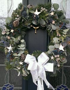 a wreath with white bows and pine cones is hanging on the front door to welcome guests