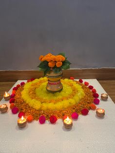 an arrangement of flowers and candles on a white table cloth with yellow petals in the center