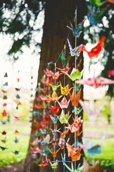 colorful paper cranes hanging from a tree in a park