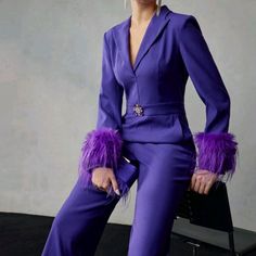 a woman in a purple suit sitting on a chair with her hands on her hips