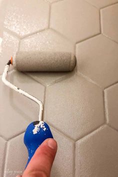 a hand is holding a paint roller in front of a white tile wall with hexagonal tiles