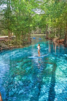 a person standing on a surfboard in the middle of a river with blue water