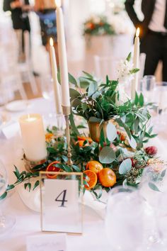 the table is set with candles, flowers and fruit for an elegant wedding reception in white linens