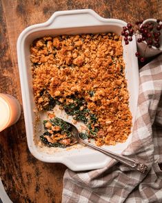 a casserole dish with spinach and crumbs on top next to a lit candle