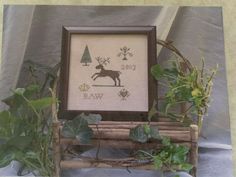 a cross - stitch picture is displayed in front of some plants and a wooden sleigh