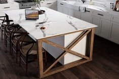 a kitchen with white cabinets and marble counter tops, an open laptop on the island