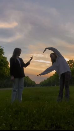 two people standing in the grass with their arms spread out and one person reaching for something