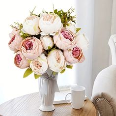 a vase filled with pink and white flowers on top of a table next to a cup