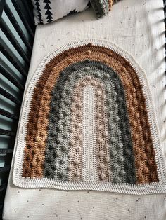 a crocheted rug with a rainbow in the middle on top of a bed