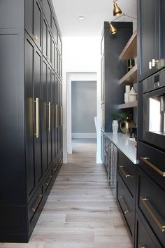 a long narrow kitchen with black cabinets and gold pulls on the doors, along with wooden flooring