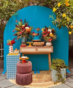 a table with flowers on it in front of a blue wall and potted plants