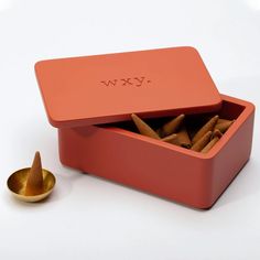 an orange box filled with cinnamons next to a small gold cup on a white surface