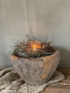 a stone bowl with some branches in it and a lit candle inside the bowl, on top of a wooden table