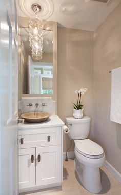 a white toilet sitting next to a sink under a bathroom mirror with a light hanging above it