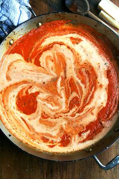 a pan filled with sauce and cheese on top of a wooden table next to utensils