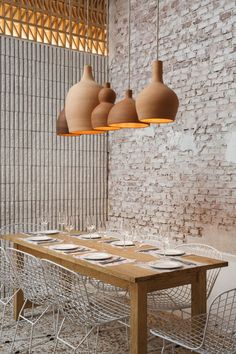 a wooden table surrounded by white chairs and hanging vases over it's head