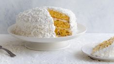 a cake with white frosting on a plate next to a fork and another slice