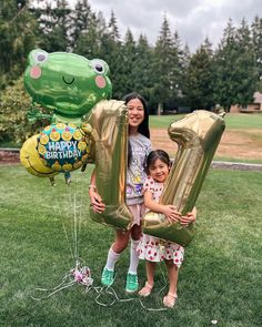 two girls holding up large balloons in the shape of numbers 20 and a frog balloon