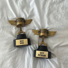 two black and gold award plaques on a white sheet with the words best wife and best husband