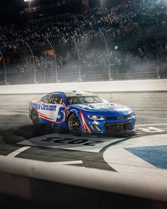 a blue and white car driving on top of a race track with people in the stands