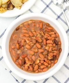 two white bowls filled with beans next to some potato wedges on a blue and white checkered table cloth