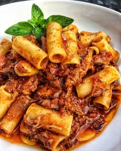 pasta with meat and tomato sauce in a white bowl on a black counter top, garnished with green leaves