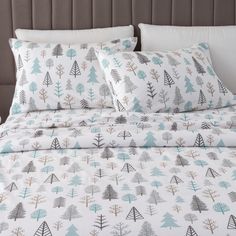 a bed covered in white and blue sheets with trees printed on the comforter cover