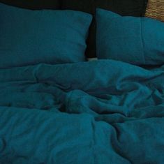 an unmade bed with dark blue sheets and pillows on top of the headboard