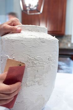 a person holding a piece of paper in front of a large white vase on a table