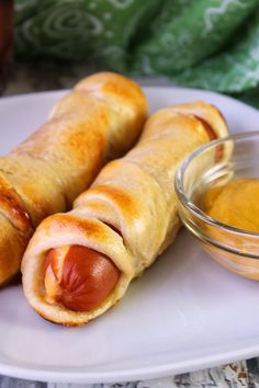 two hotdogs on a plate with mustard and ketchup in a bowl