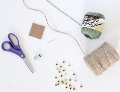 yarn, scissors and other crafting supplies laid out on a white surface with pins