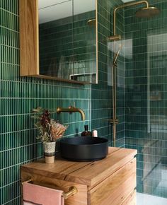 a bathroom with green tiled walls and wooden cabinet, black bowl sink and gold faucet