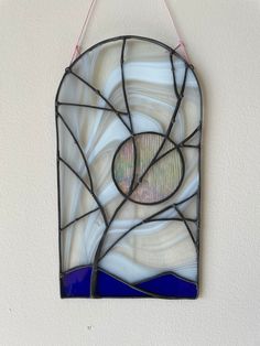 a blue and white stained glass window hanging on a wall with string attached to it