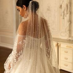 a woman in a wedding dress with a veil on her head is looking down at the floor