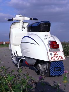 a white scooter is parked on the side of the road near some flowers