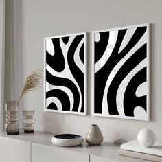 two black and white paintings hanging on the wall above a buffet table with vases