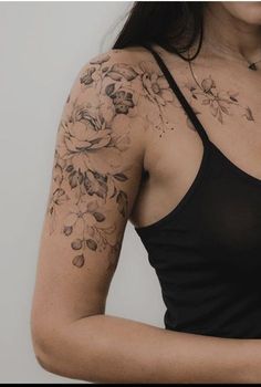 a woman wearing a black tank top with flowers on her arm and shoulder tattoo design