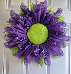 a purple and green mesh wreath hanging on a white door with lavender flowers in the center