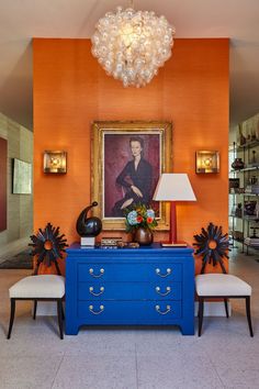 an orange room with a blue dresser and two white stools in front of a painting