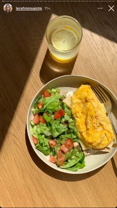 there is a plate with salad and an omelet on it next to a glass of water