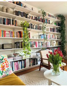 a living room filled with lots of books and furniture next to a wall mounted book shelf